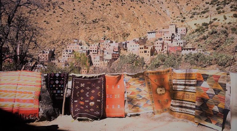 Handwoven Berber rugs displayed in front of a mountain village